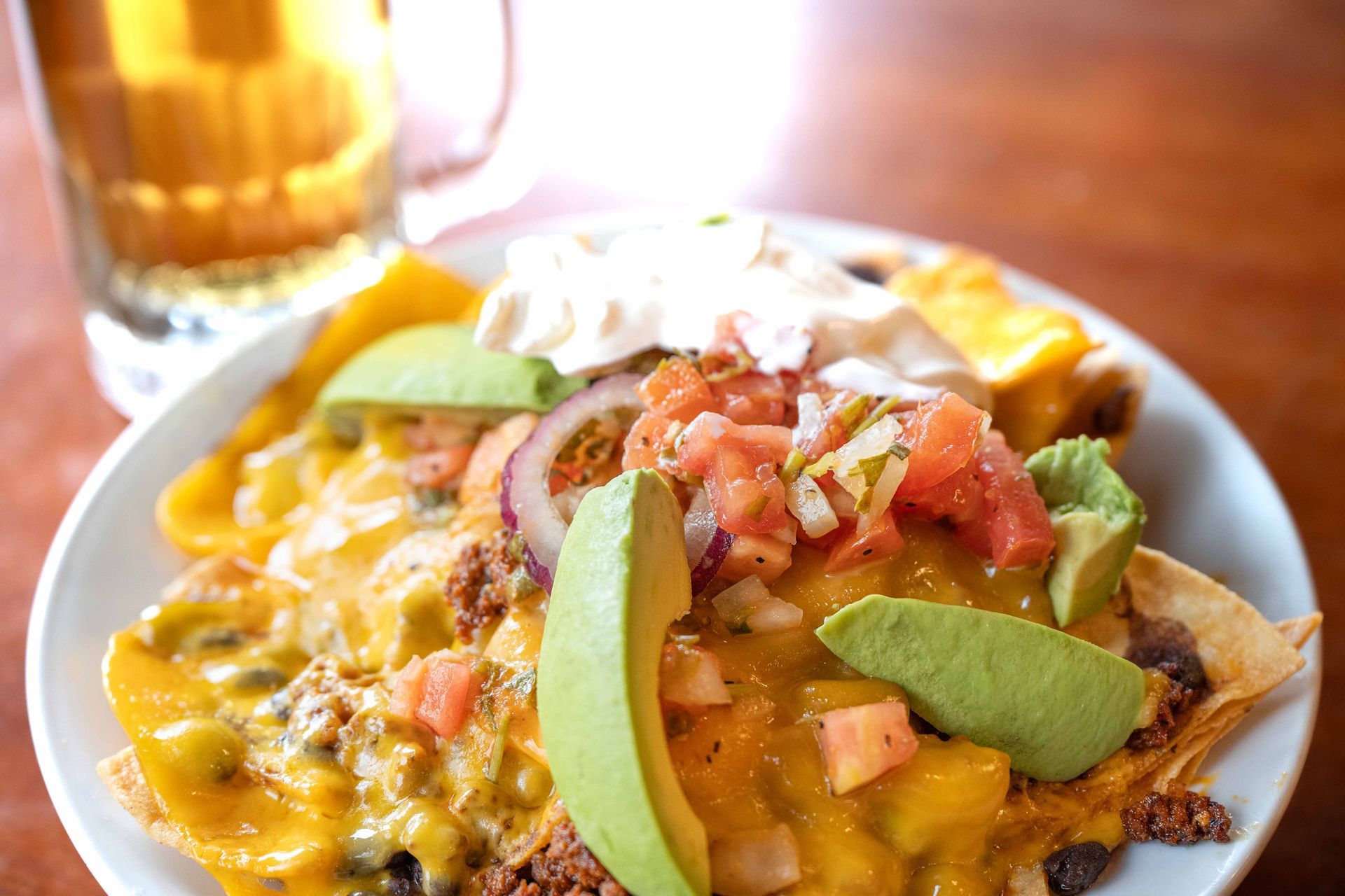Cheesy nachos topped with avocado and pico de gallo on a white plate beside a drink