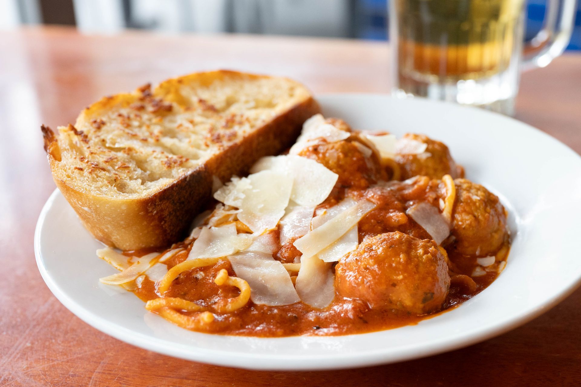 Plate of pasta in red sauce topped with shaved cheese, served with garlic bread on a table