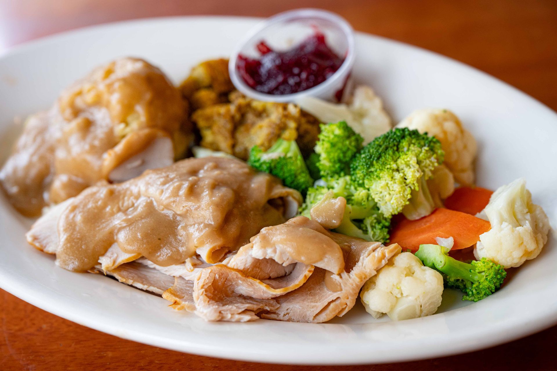 Plate of sliced turkey with broccoli, cauliflower, carrots, and cranberry sauce