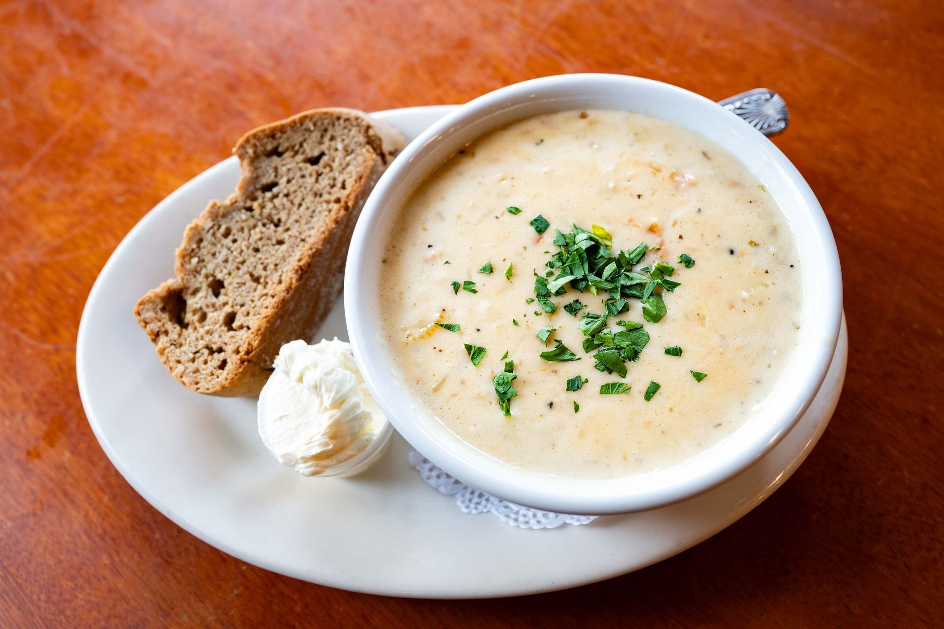 Bowl of creamy soup with herbs, bread slices, and a dollop of cream on a white plate