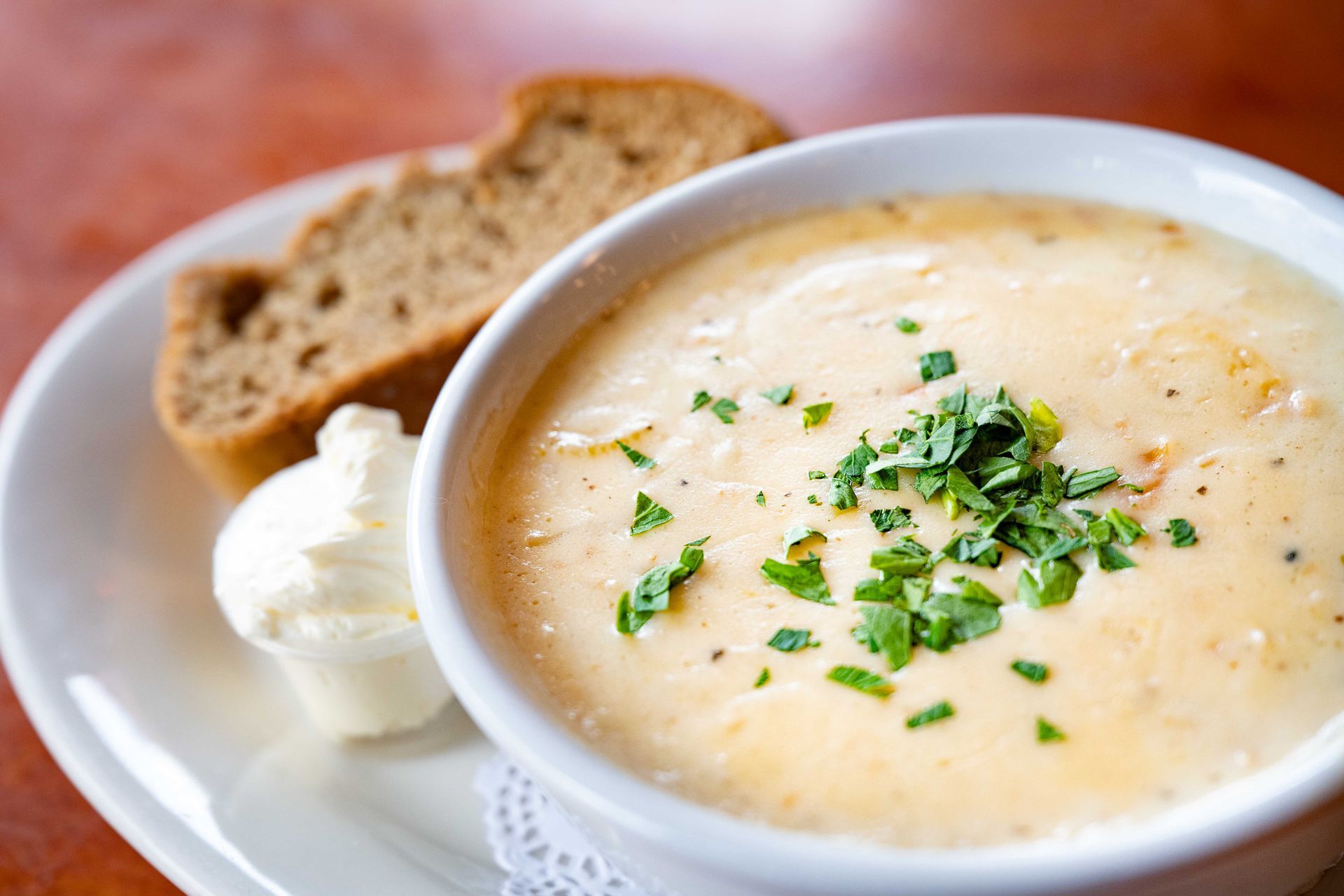 Creamy soup in a white bowl topped with herbs, served with bread and butter