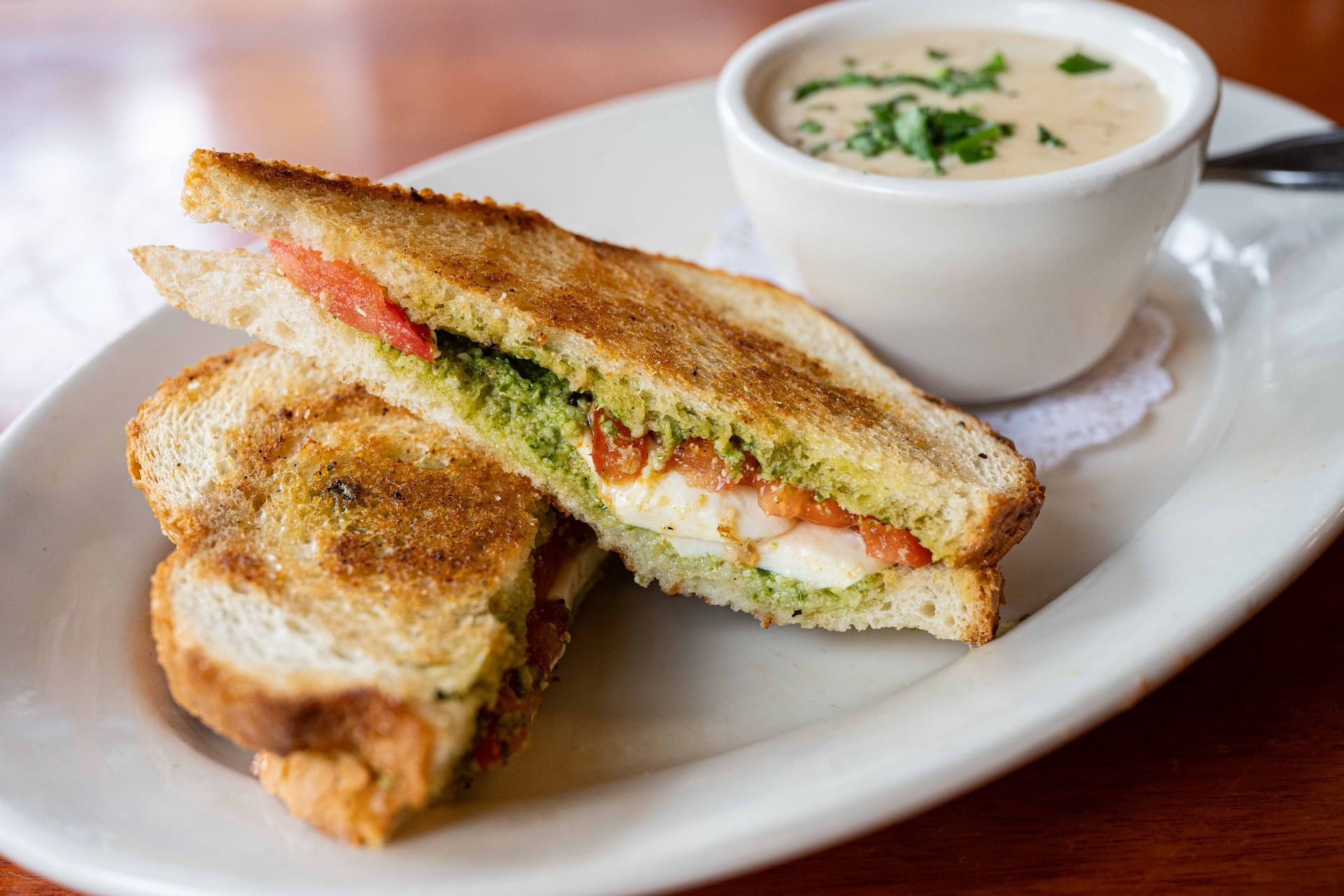 Grilled sandwich halves on a white plate with a bowl of creamy soup and herbs
