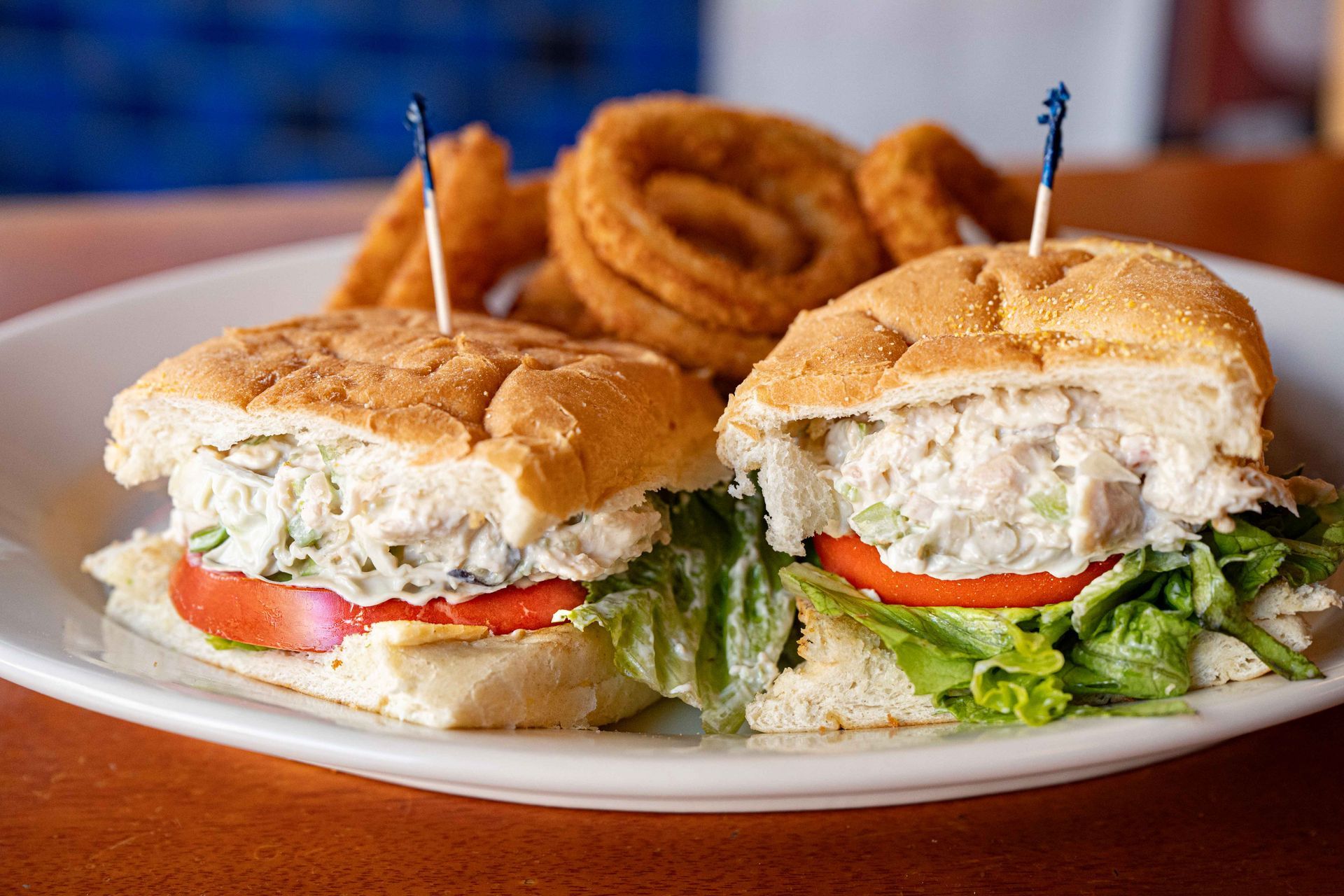 Two sandwiches with lettuce and tomato on a white plate, topped with onion rings and toothpicks