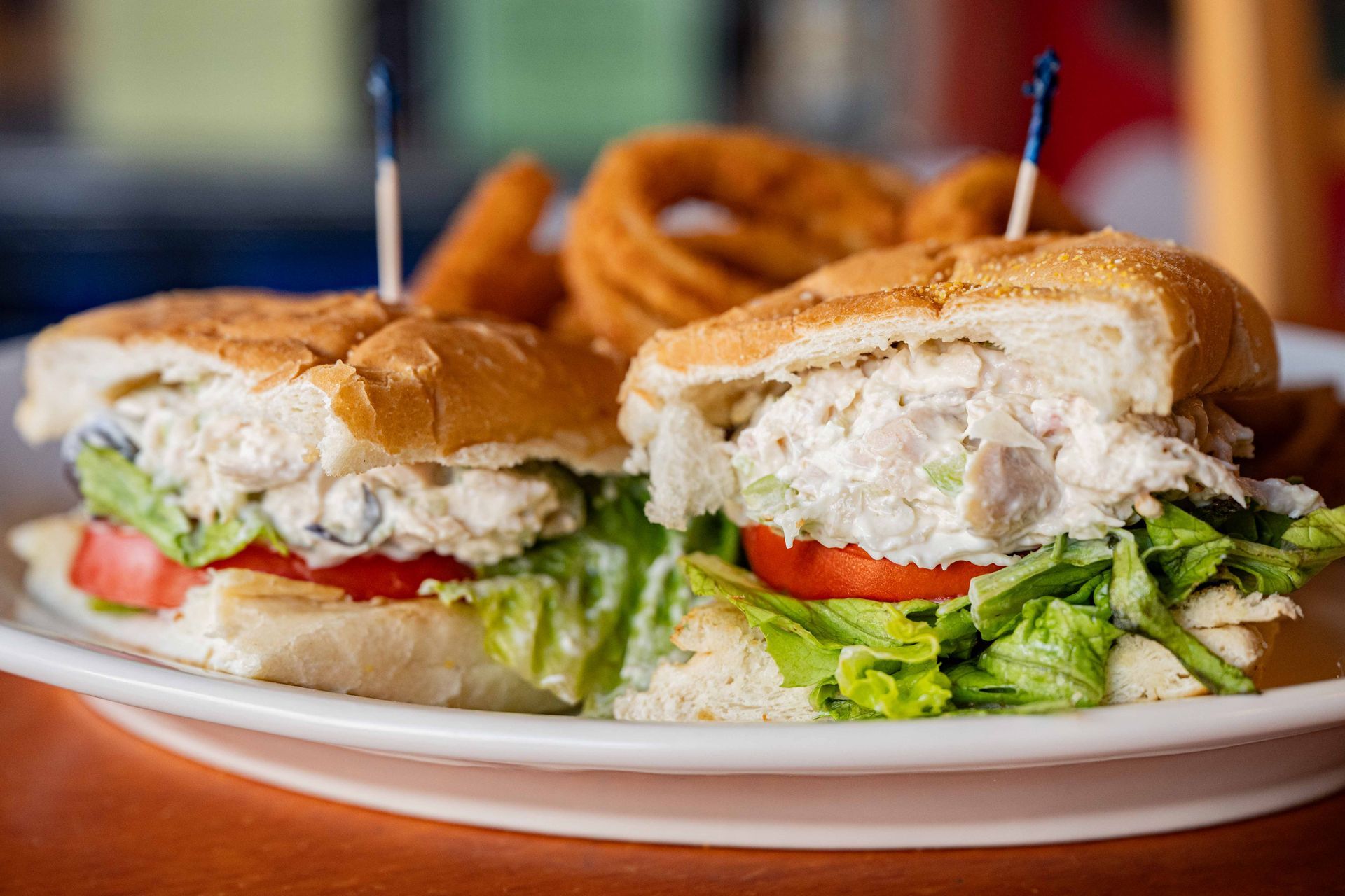 Two tuna salad sandwiches with lettuce and tomato on a white plate