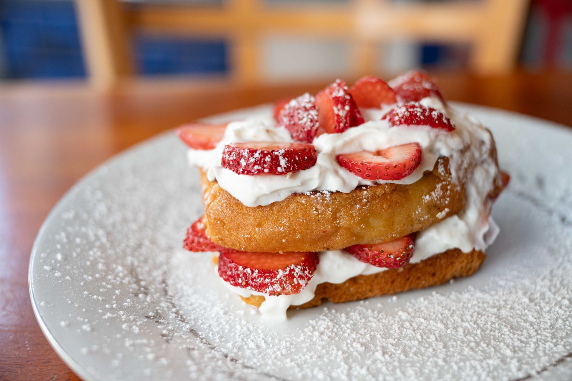Stacked strawberry dessert with whipped cream on a white plate, dusted with powdered sugar