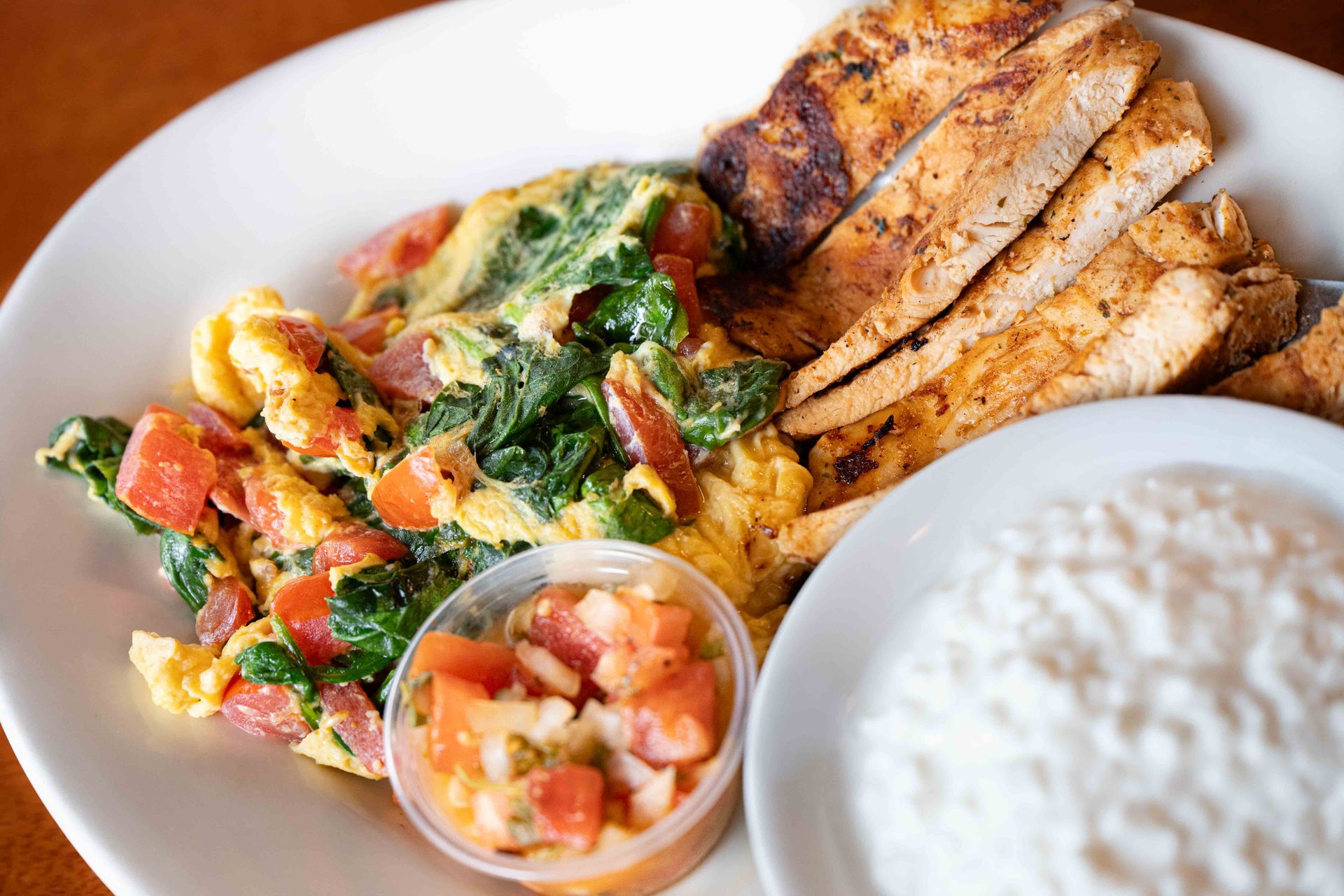 Grilled chicken, scrambled eggs, salsa, and rice on a white plate