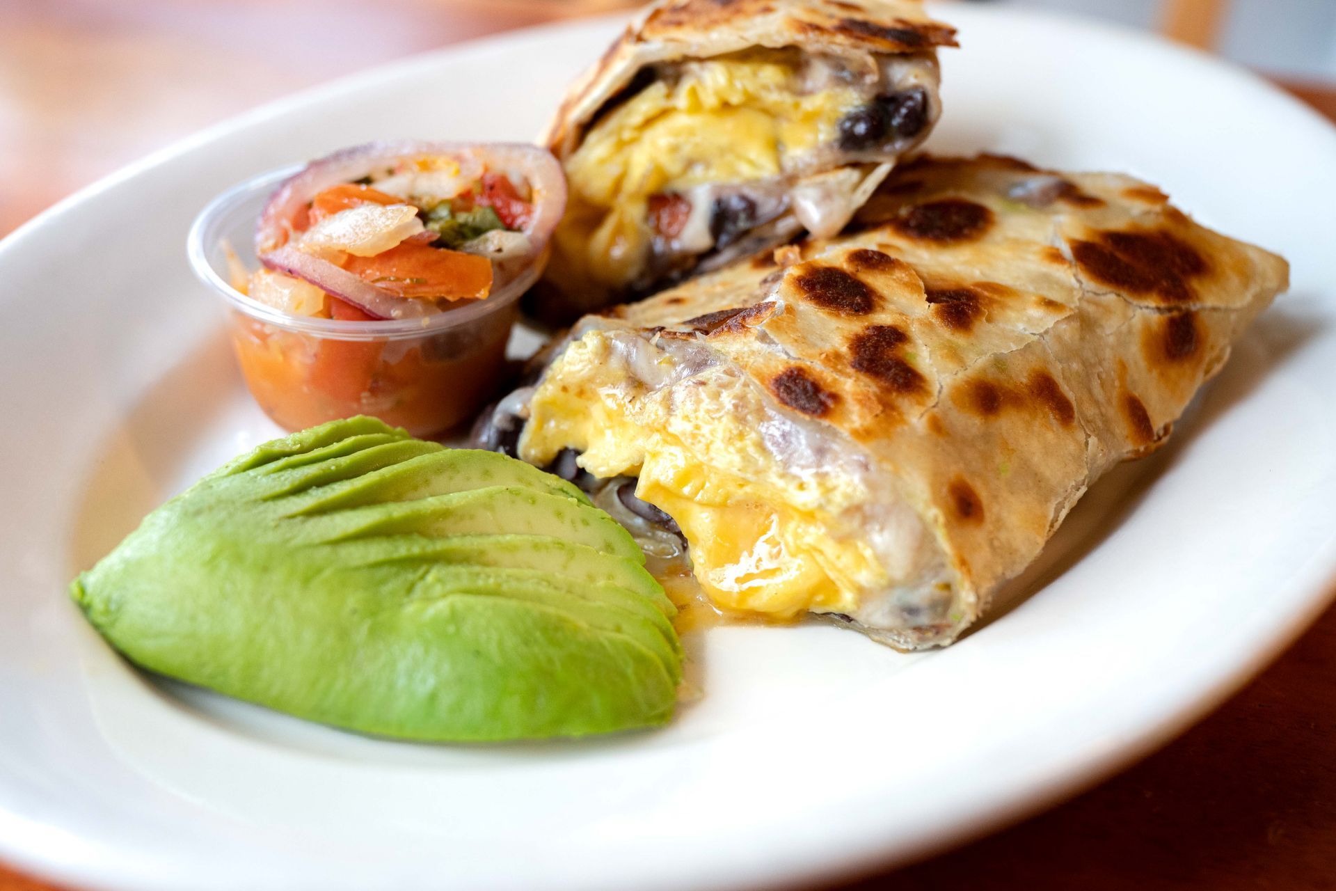 Plate with a stuffed burrito, avocado slices, and salsa on a white dish