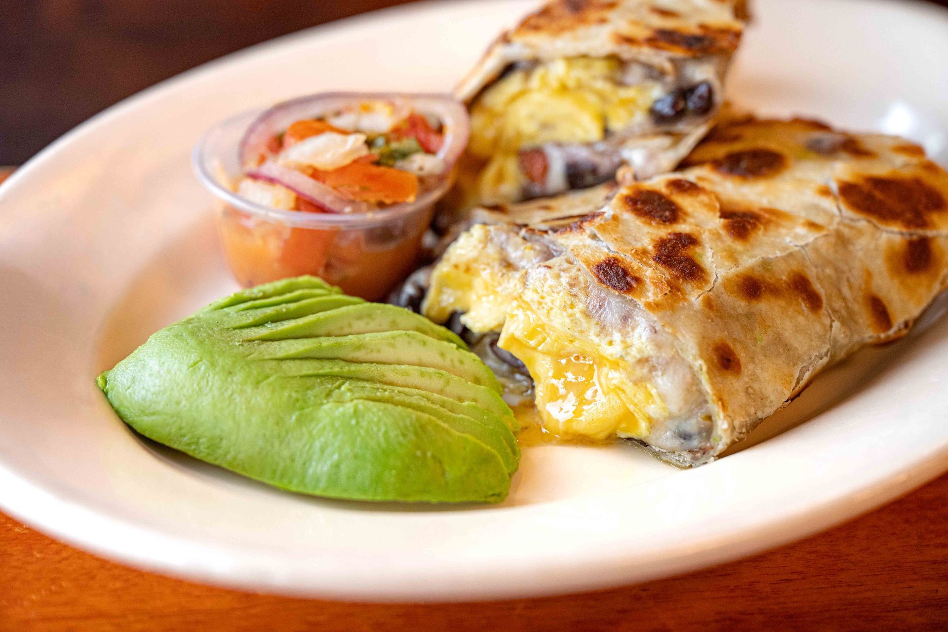Quesadilla on a white plate with avocado slices and salsa cup
