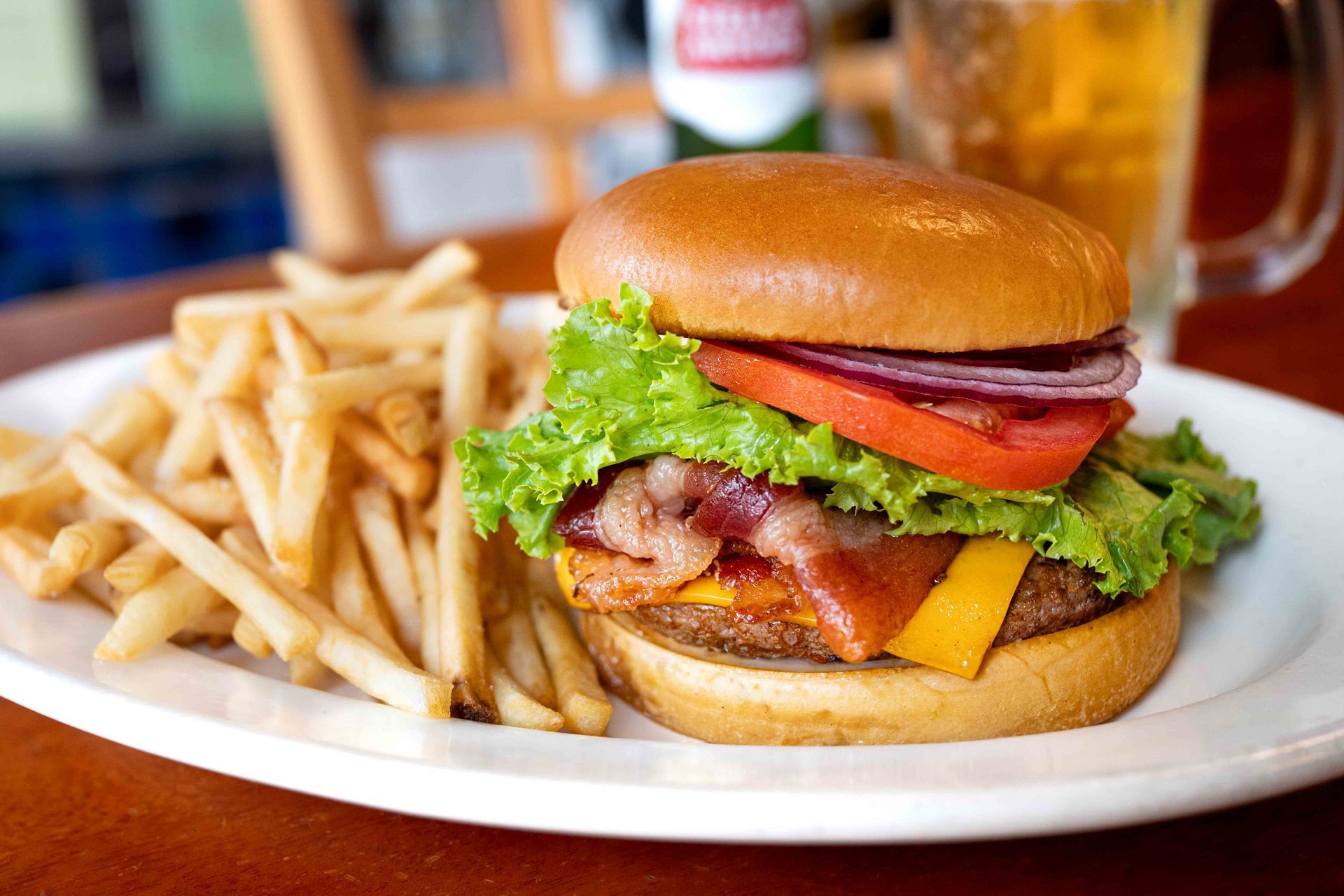 Burger with lettuce, tomato, bacon, cheese, and fries on a white plate in a restaurant