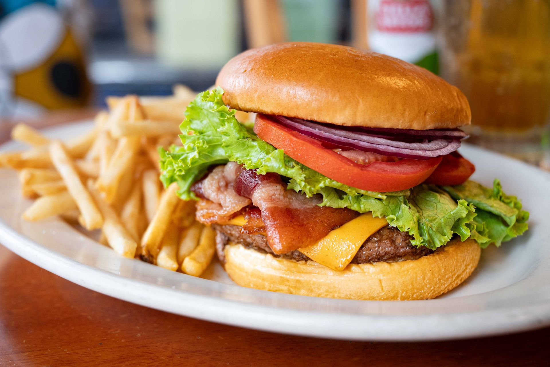Bacon cheeseburger with lettuce and tomato on a plate with fries in the background
