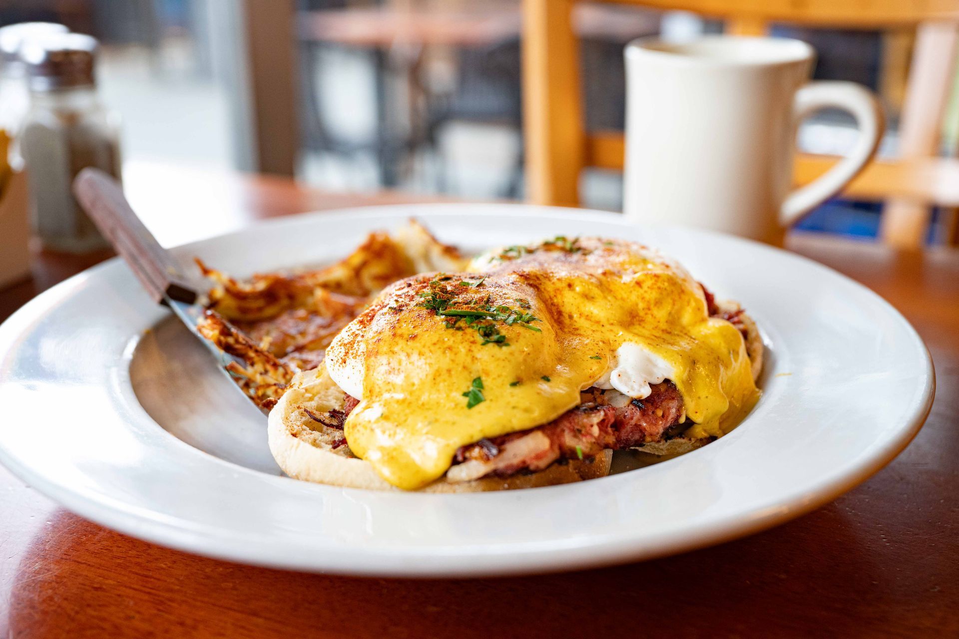 Poached eggs on toast with hollandaise on a white plate beside a coffee mug
