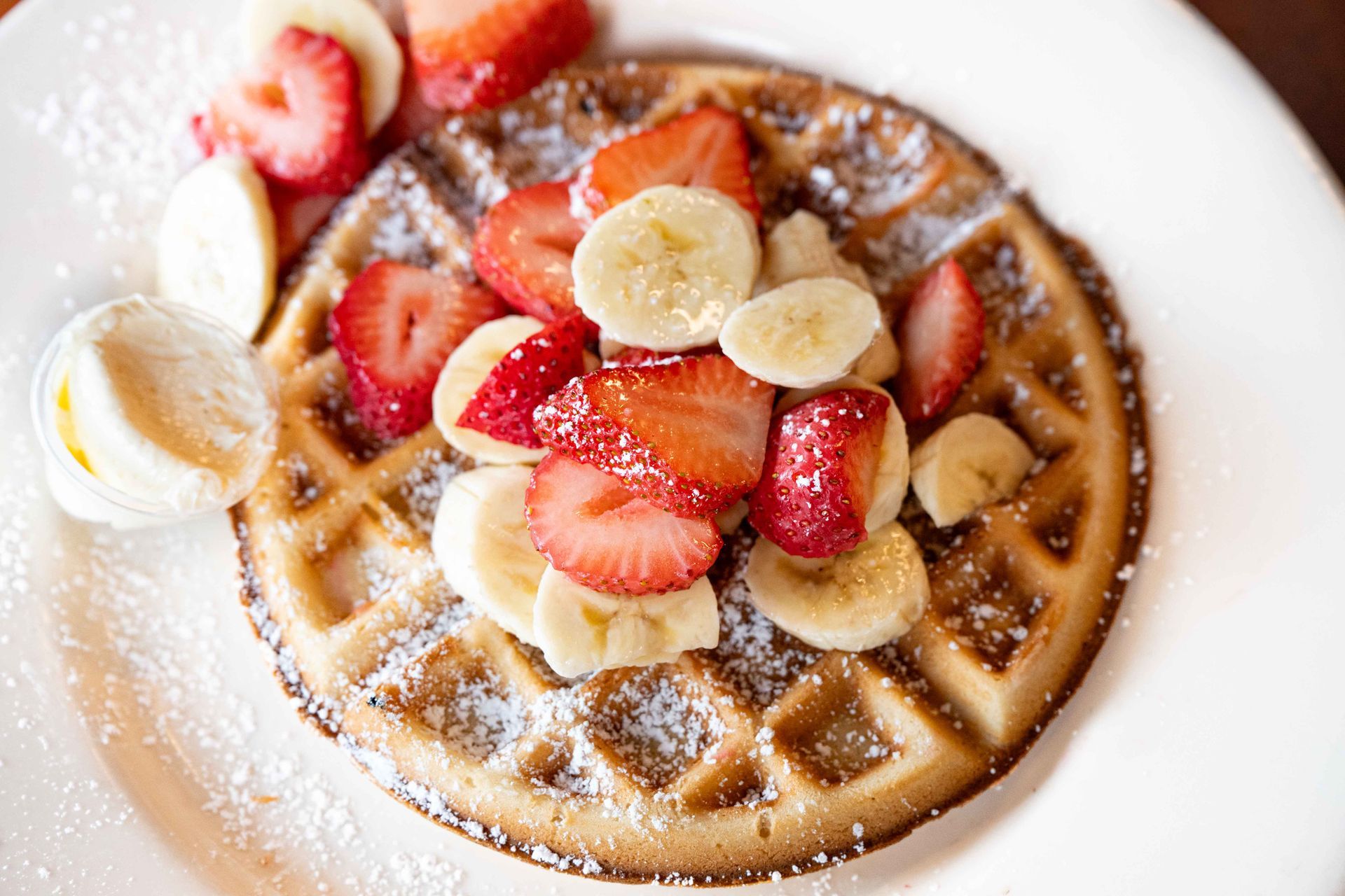 Waffle topped with strawberries, banana slices, and powdered sugar on a white plate