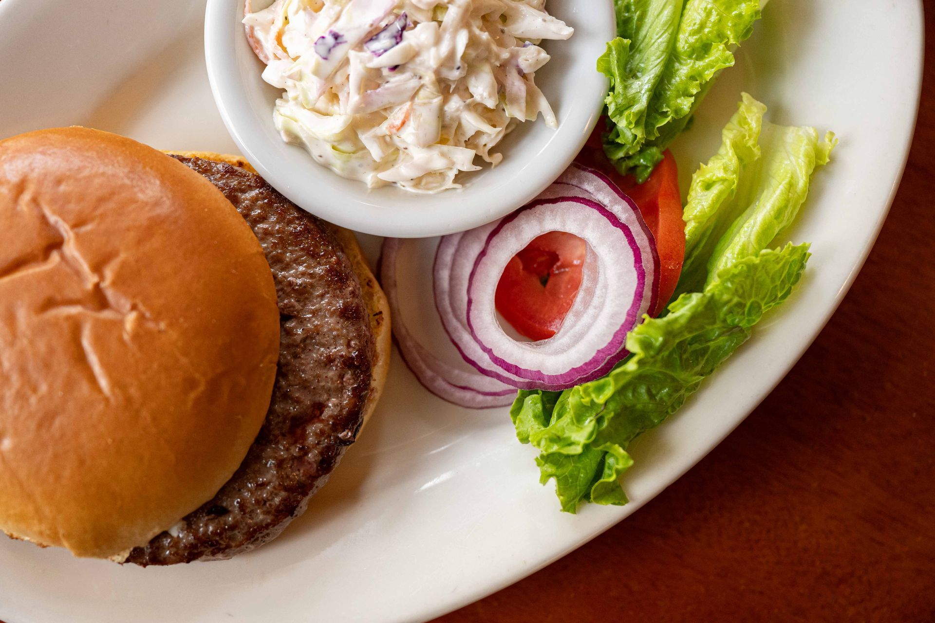 Burger plate with coleslaw, lettuce, and red onion slices on a white dish