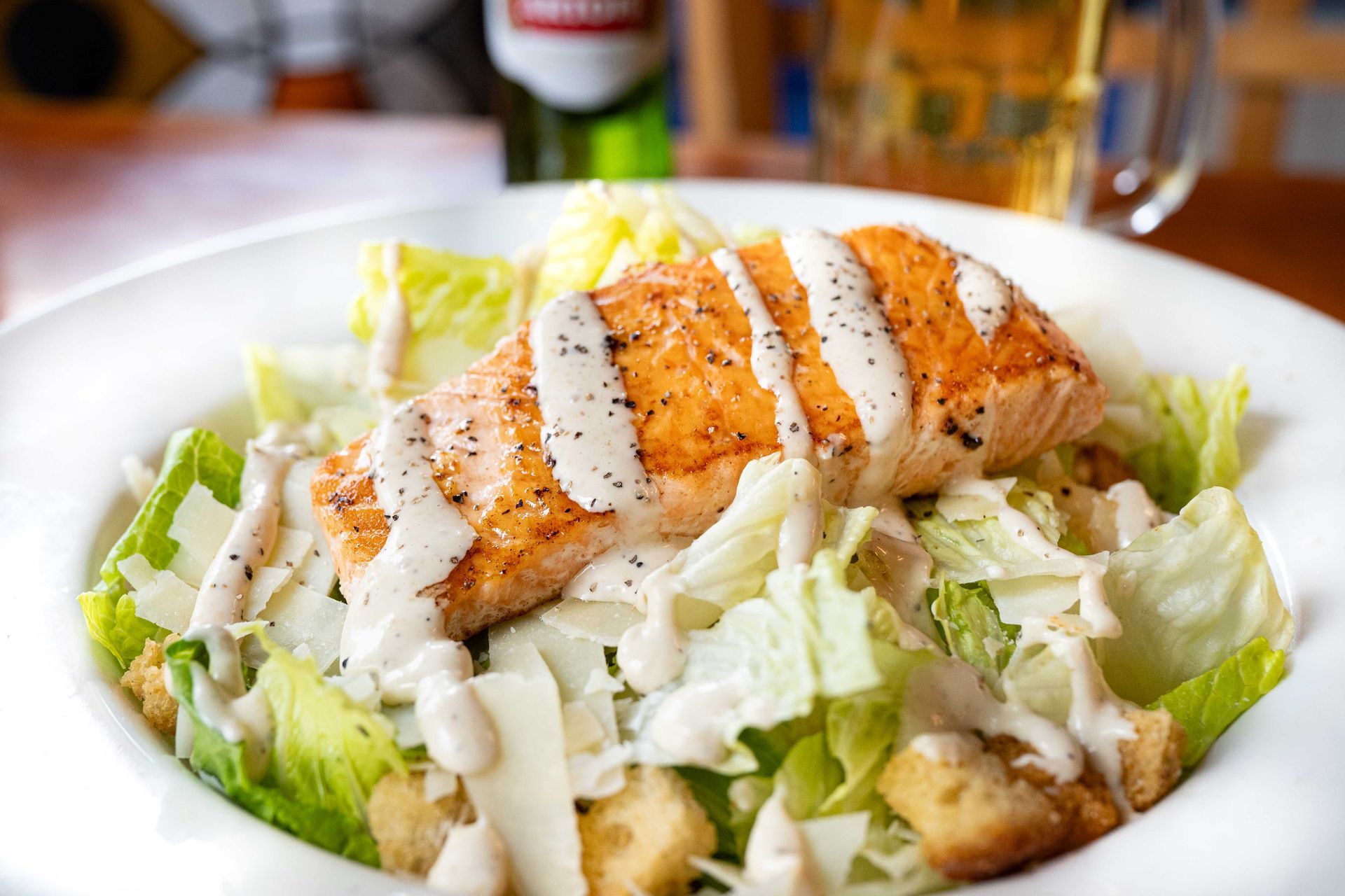 Grilled salmon Caesar salad with croutons and white dressing on a white plate