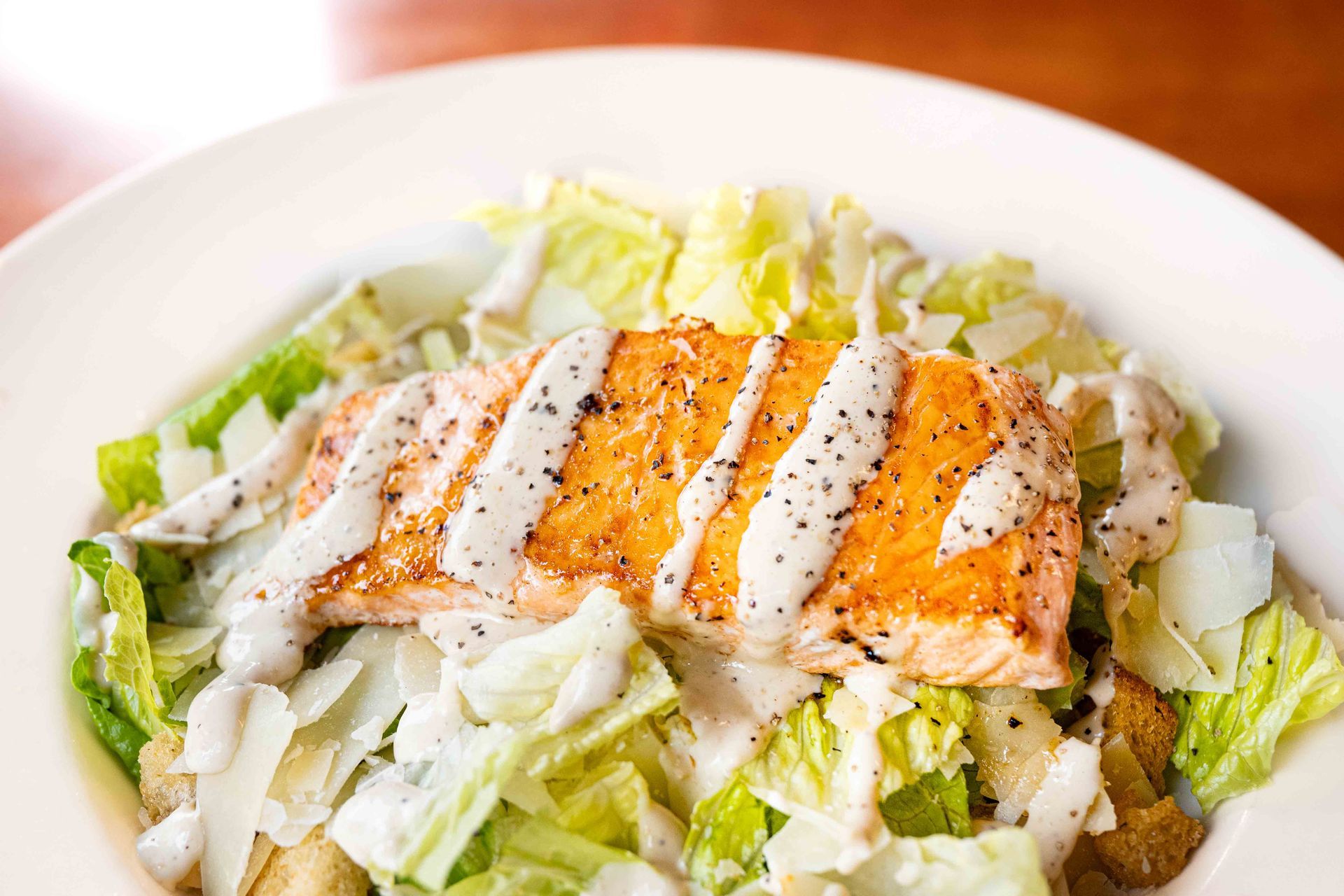 Grilled salmon on chopped romaine salad with creamy dressing on a white plate
