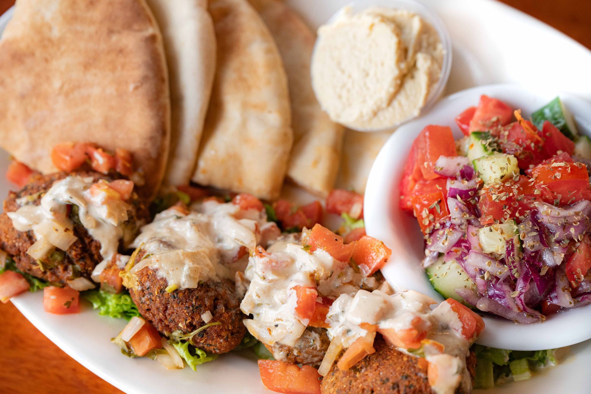 Mediterranean spread with pita bread, falafel topped with sauce, hummus, and a fresh diced tomato salad