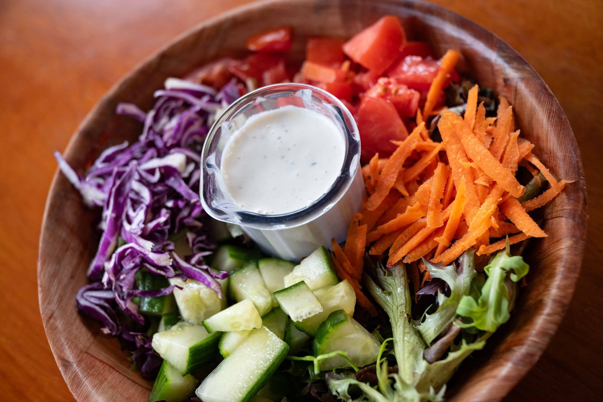 Colorful salad bowl with cucumbers, shredded carrots, purple cabbage, greens, and creamy dressing in the center