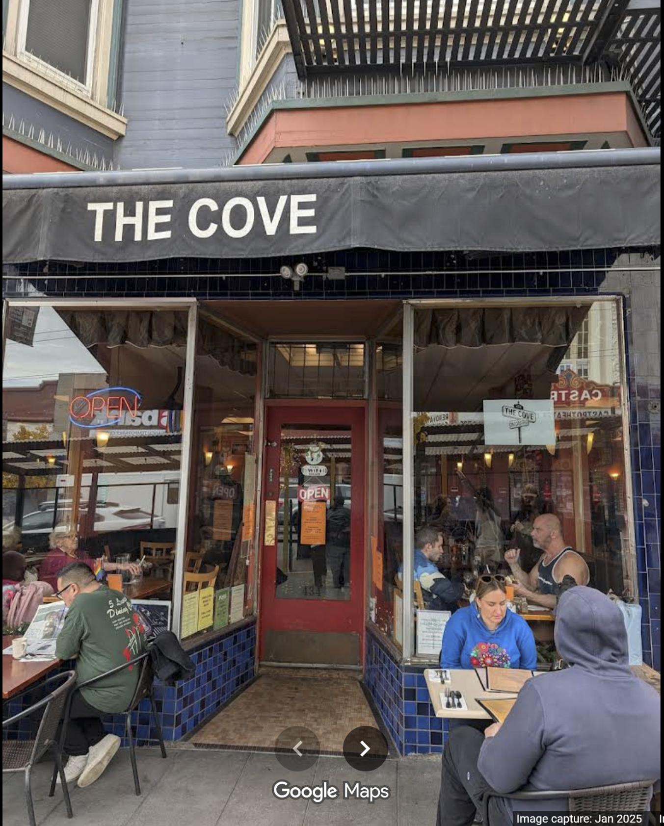 Cafe storefront with black awning reading “THE COVE,” open entrance, and people seated outside at tables