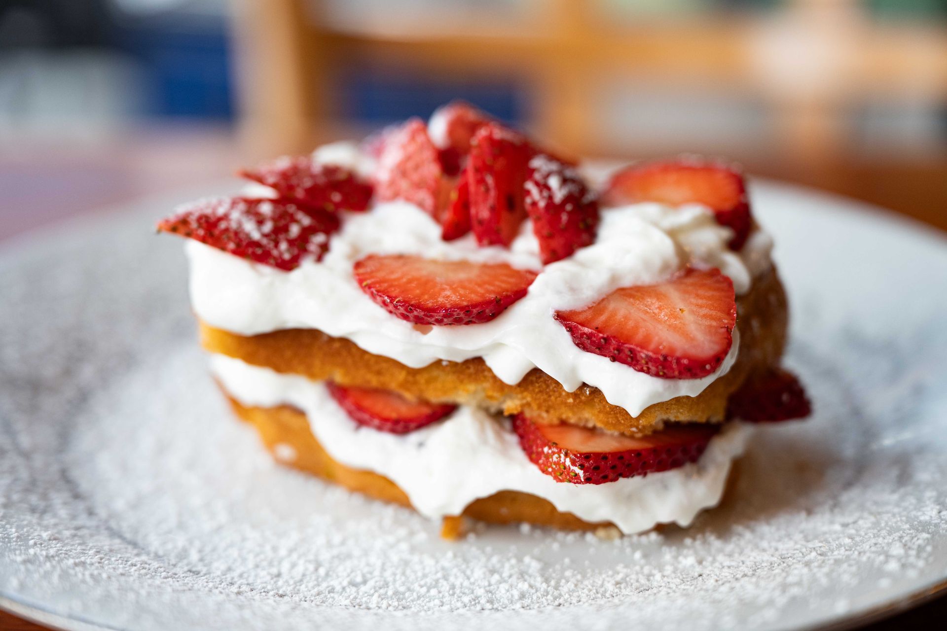 Strawberry shortcake with whipped cream on a white plate, dusted with powdered sugar.