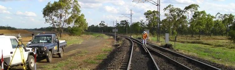 A white truck is parked on the side of a train track.