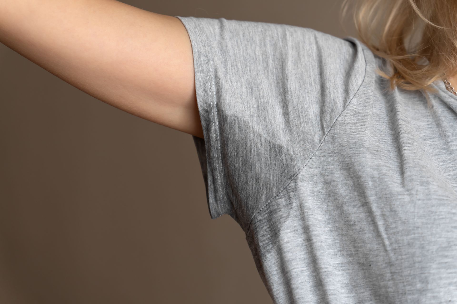 Un gros plan de l'aisselle moite d'une femme portant un t-shirt gris.