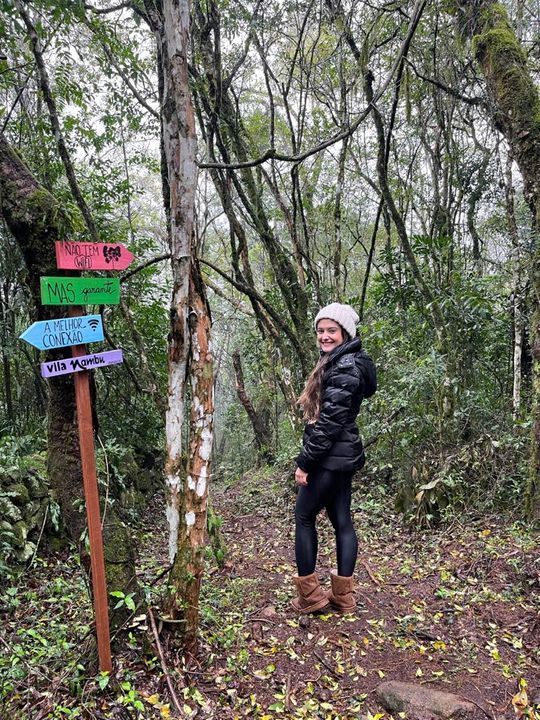 Uma mulher está parada ao lado de uma placa na floresta.