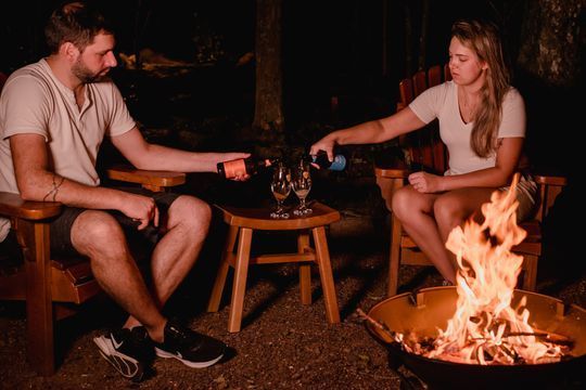 Um homem e uma mulher estão sentados ao redor de uma fogueira bebendo vinho.