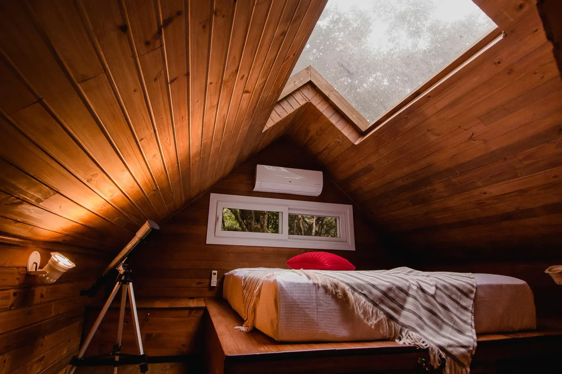 Um quarto com cama e telescópio no sótão.