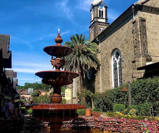 Uma fonte em frente a uma igreja com uma torre do relógio ao fundo.