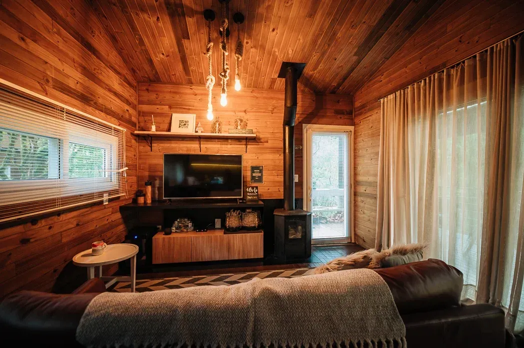 Uma sala de estar em uma cabana de madeira com sofá, televisão e lareira.