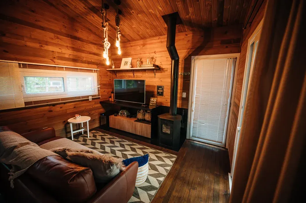 Uma sala de estar em uma cabana de madeira com sofá, televisão e lareira.