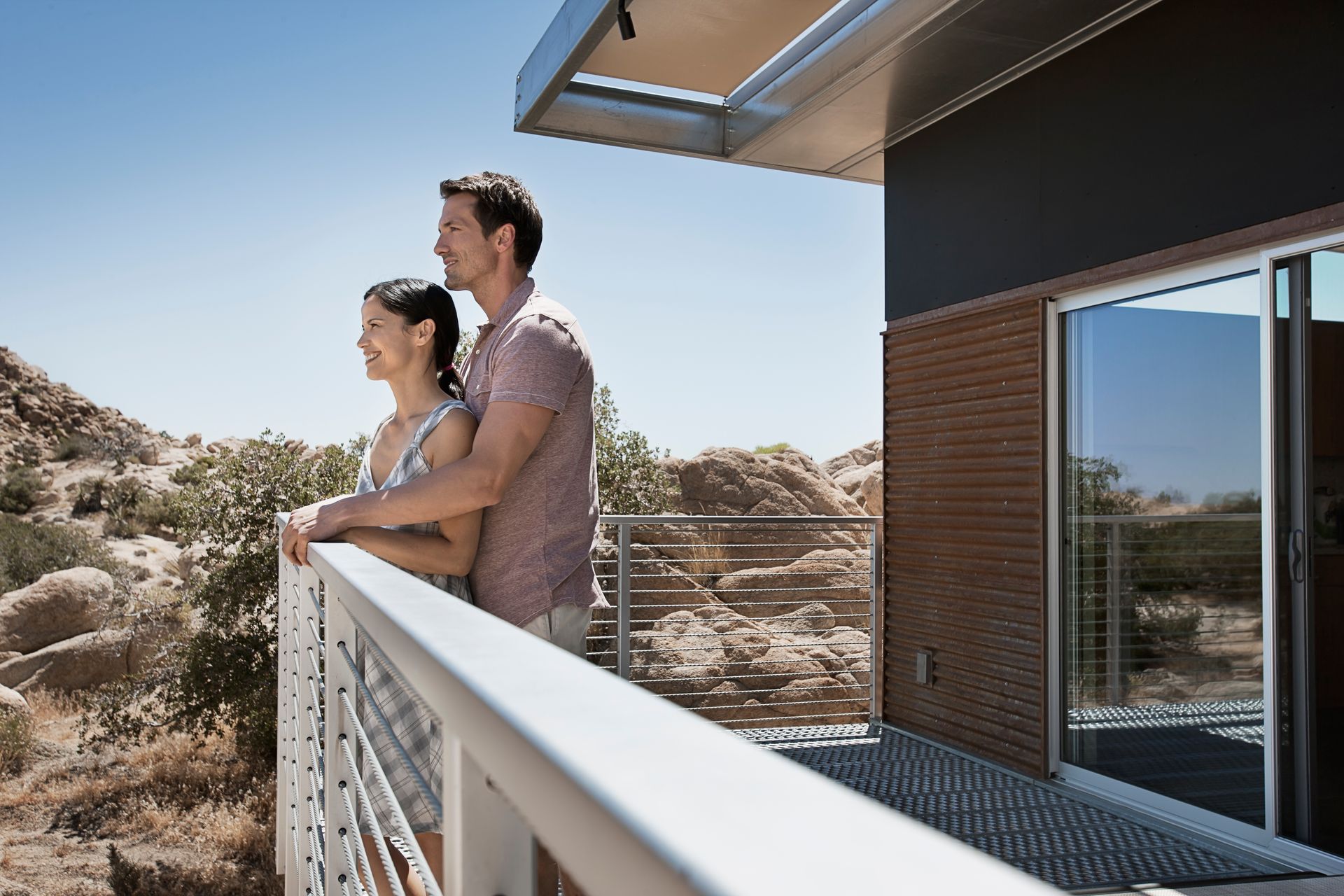 A man and a woman are standing on a balcony looking out over a desert landscape.