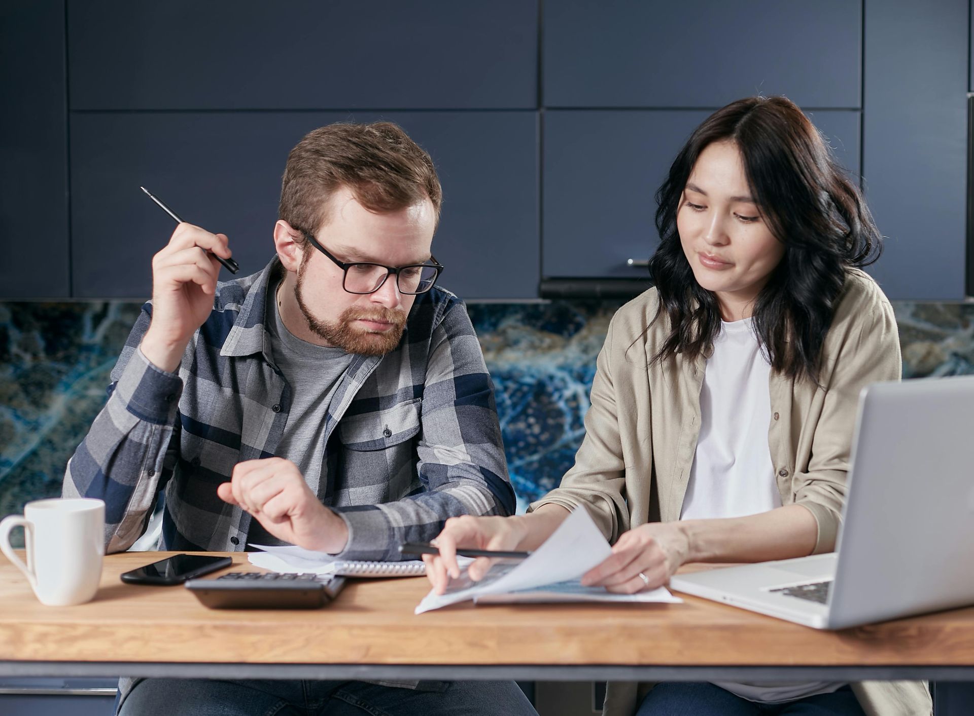 A man and a woman are sitting at a table looking at papers and a laptop.