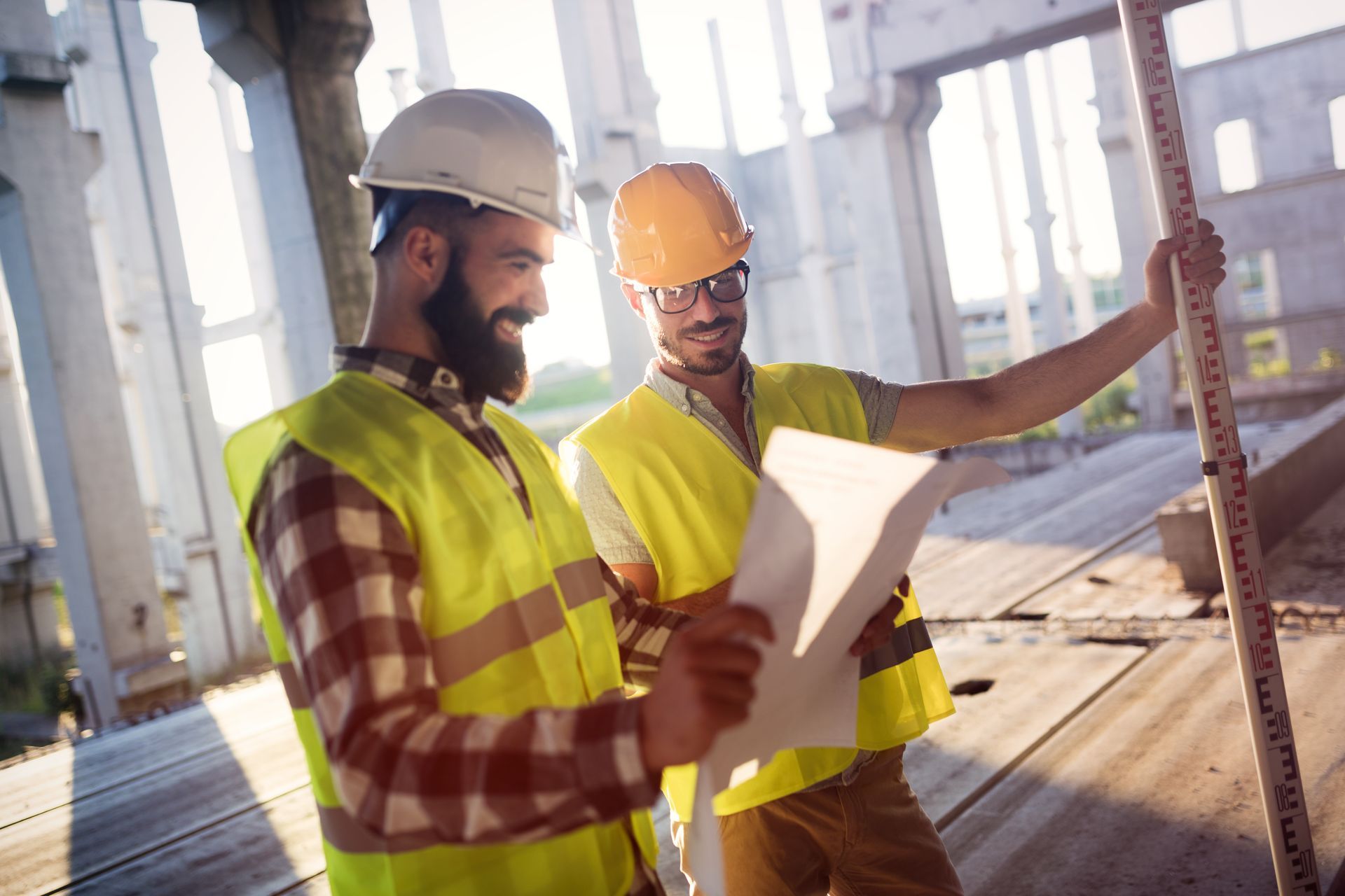 Two construction workers are looking at a blueprint on a construction site.