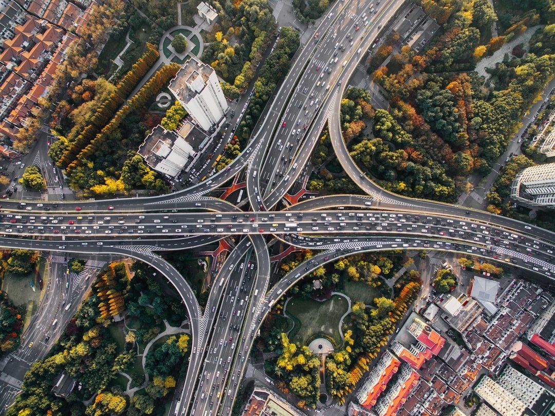 Aerial view of a complex highway interchange with cars, surrounded by buildings and trees.