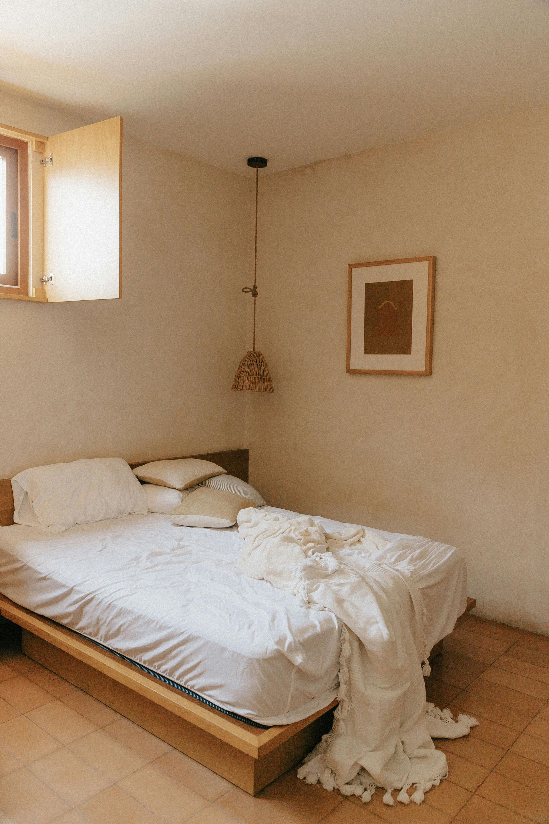 Bedroom with a wooden bed frame, white bedding, and a decorative light fixture hanging from the ceiling.