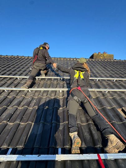 Powersave Company, gehuld in veiligheidsharnassen, installeren zonnepanelen op een dak. Zonnige dag, heldere blauwe lucht.