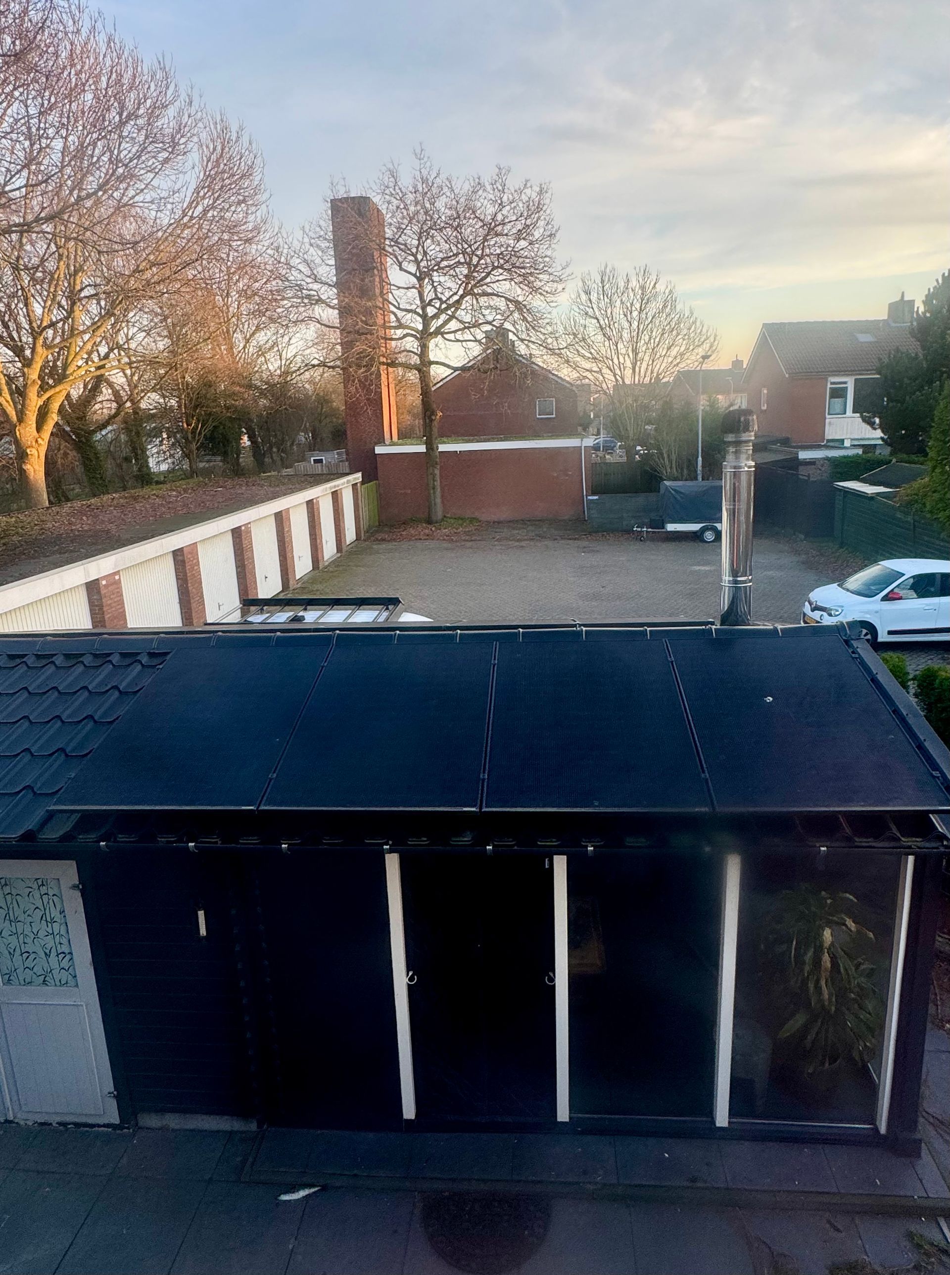 Uitzicht op een parkeerplaats, een rode bakstenen muur en een gebouw, en een hoge schoorsteen met een zwart dak op de voorgrond.