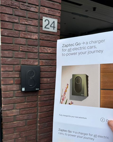 Een laadpaal voor elektrische voertuigen op een bakstenen muur met een bordje. Het nummer 24 is erboven zichtbaar.