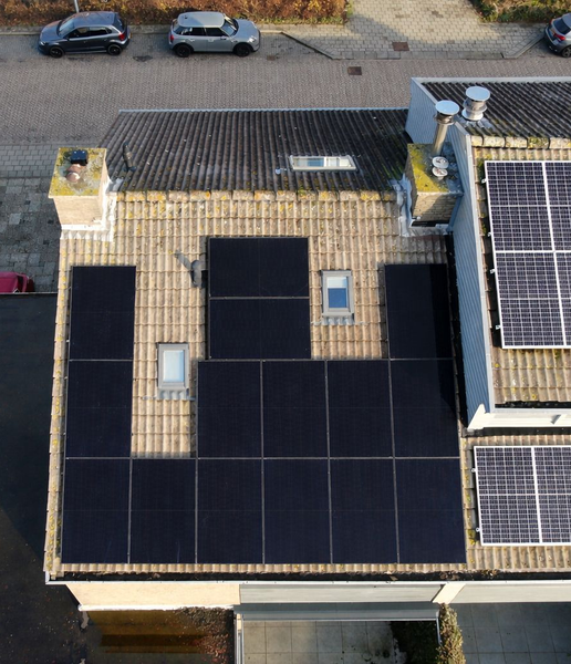 Twee verdiepingen tellende rijtjeshuizen met zonnepanelen op het dak, een auto ervoor geparkeerd, verlicht door de zonsondergang.