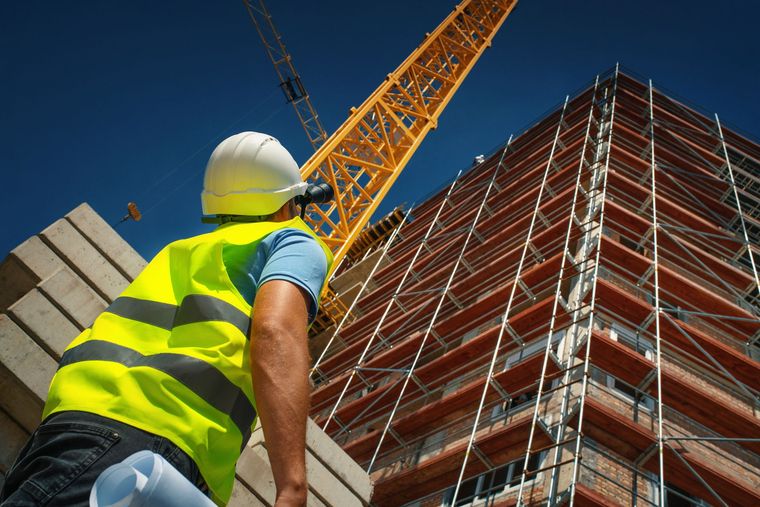 Un operaio edile è in piedi davanti a un edificio in costruzione.