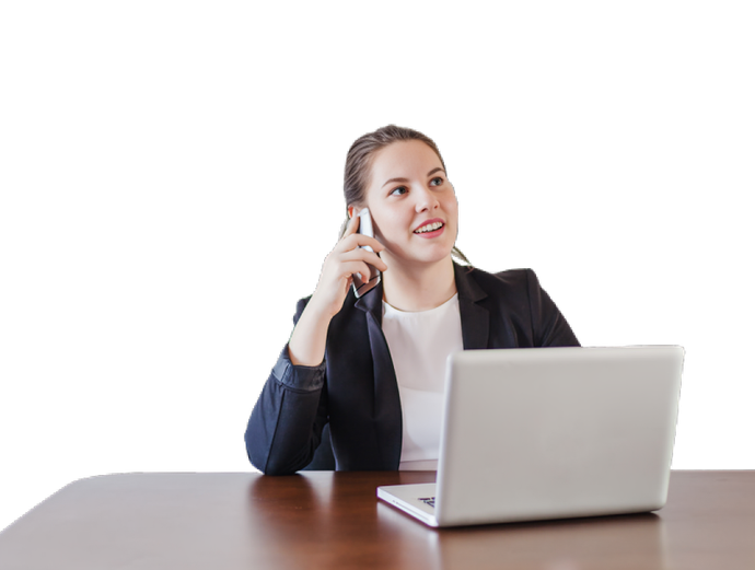 A woman is sitting at a desk with a laptop and talking on a cell phone.