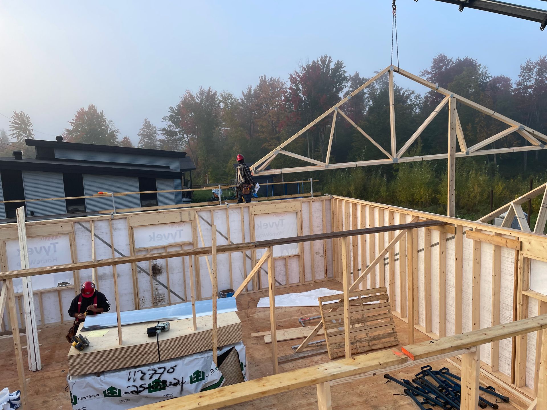 Une grue soulève une structure en bois au sommet d'un bâtiment en construction.