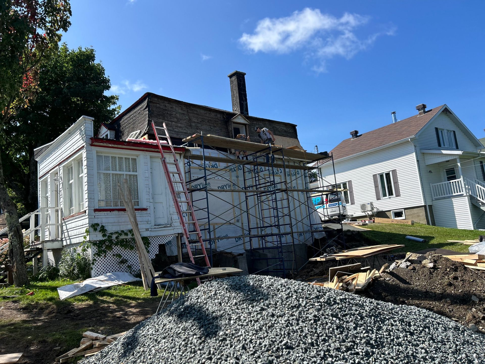 Une maison blanche avec un échafaudage autour et un tas de gravier devant.