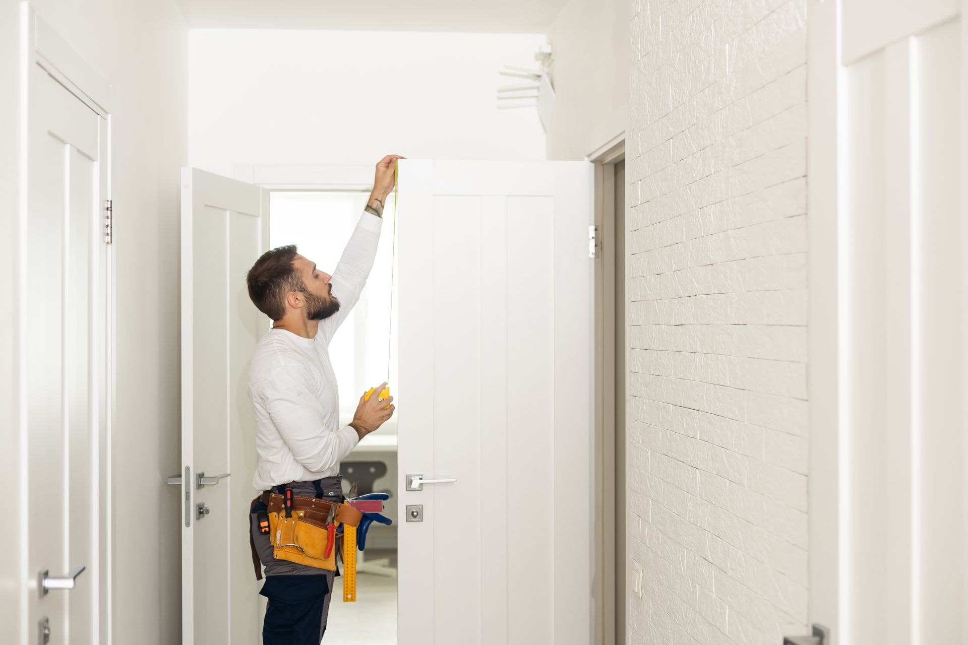 A man is measuring a wall with a tape measure in a hallway