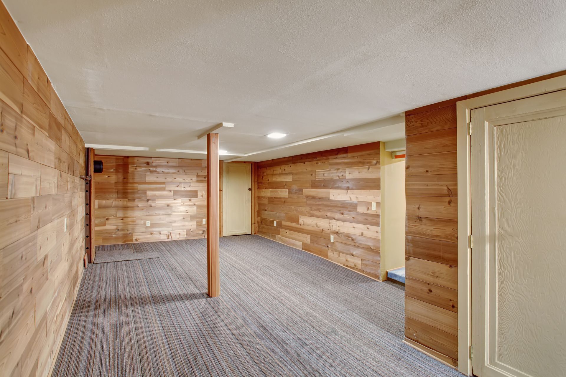 An empty basement with wooden walls and a carpeted floor