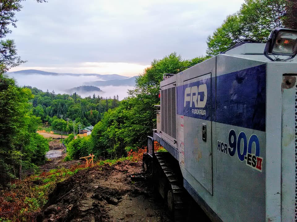 Générateur à flanc de colline surplombant une vallée brumeuse. Arbres verts et ciel couvert.