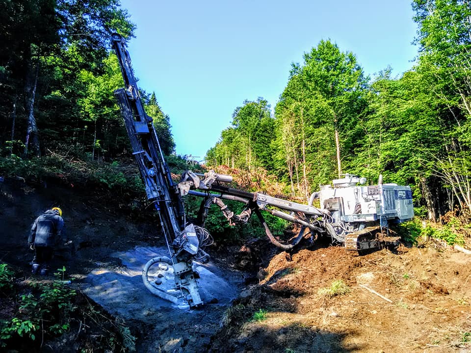 Une foreuse sur un flanc de colline, dégageant un passage à travers une forêt ; un ouvrier portant un casque jaune.