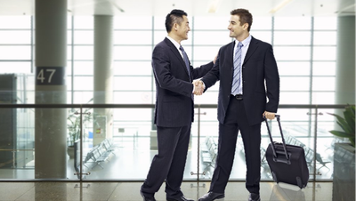 Two men in suits are shaking hands in an airport.