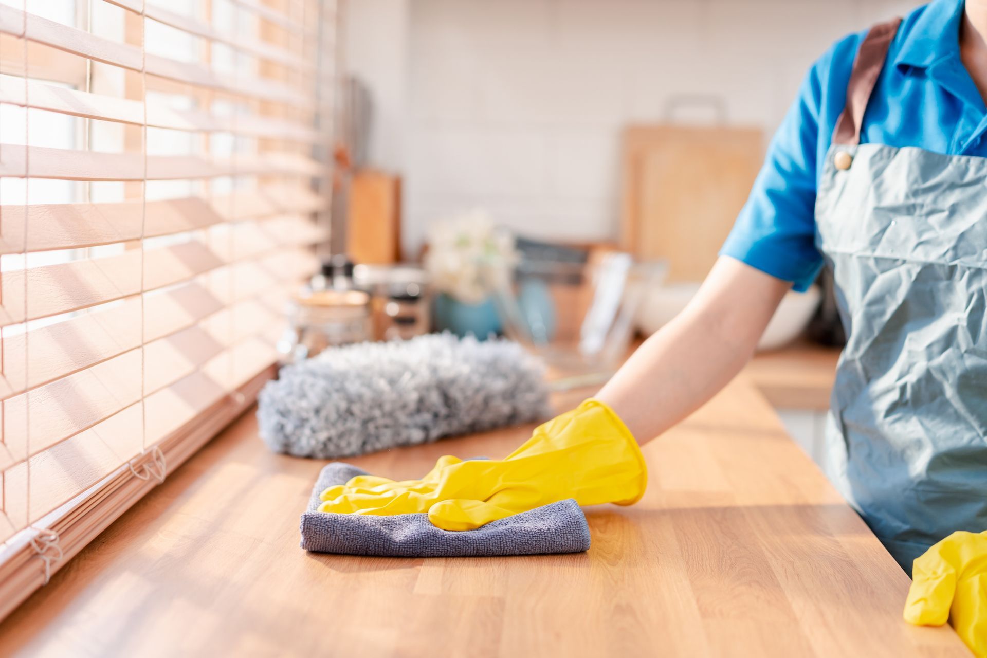 Person in yellow gloves wiping wooden counter in a kitchen.